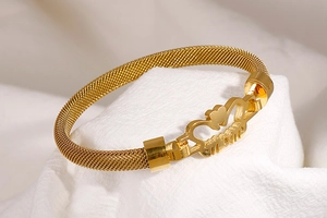 Macro detail of golden mesh bracelet featuring MOM lettering and heart-shaped accents