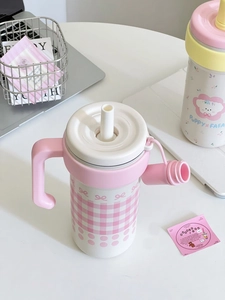 Detail of pink plaid straw cup with ergonomic handle and lid on a cozy desk setup