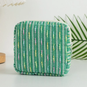 Detail of green tweed cosmetic bag featuring colorful polka dot stripes and white zipper