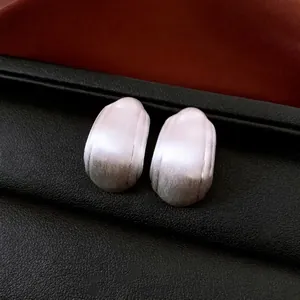 Boucles d'oreilles ovales irrégulières en argent brossé sur fond de cuir noir luxueux
