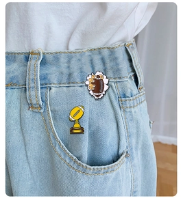 Detail showing rugby ball and trophy enamel pins on blue denim jeans pocket