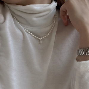 Close-up of minimalist rice pearl necklace with a teardrop zircon pendant on white sweater
