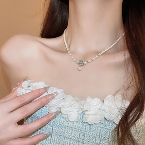 Close-up of pearl necklace with a square blue gemstone and teardrop pearl pendant