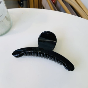 Close-up of a medium-sized glossy black curved hair claw clip on a white surface