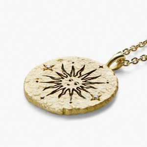 Close-up of gold coin pendant featuring sun rays, human face engraving, and small crystals
