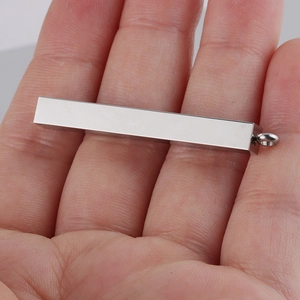 Macro detail of polished stainless steel cuboid bar pendant held in a person's hand