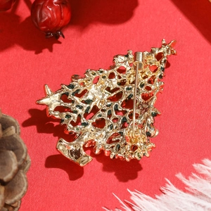 Goldene Weihnachtsbaum-Brosche mit hohlem Design und Anstecknadel auf rotem Hintergrund