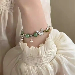 Chinese style bracelet with green jade-like beads and silver butterfly charm on wrist