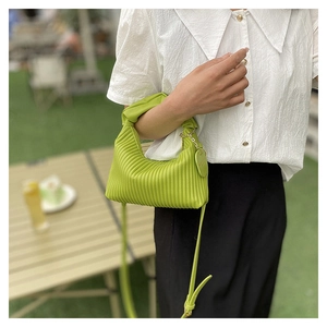 Detail of lime green pleated shoulder bag with heart charm in outdoor setting