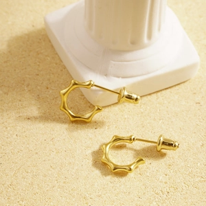 Minimalist gold stainless steel C-shaped earrings with wavy texture on a sand pedestal