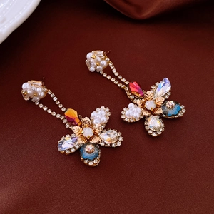 Elegant gold earrings with pearls and colorful zircons on dark velvet background