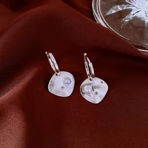 Matte silver rhombic earrings with pearl and zircon on deep red silk background