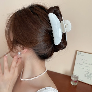 Détail d'une pince à cheveux fleur en acrylique blanc marbré portée sur un chignon élégant