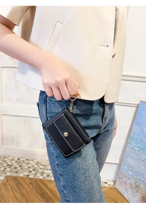 Detail of a black leather key pouch with white stitching and gold chain held by a model