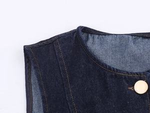 Détail du gilet en jean bleu foncé avec coutures contrastées et bouton doré poli