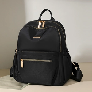 Detail of black nylon backpack featuring high-gloss gold zippers and multi-layer pockets