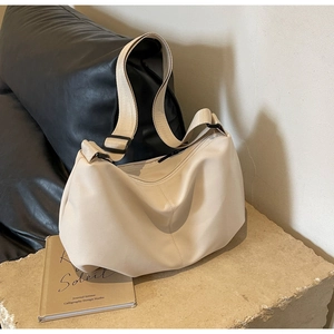 Close-up of cream-white crescent tote bag with wide adjustable strap on a stone base
