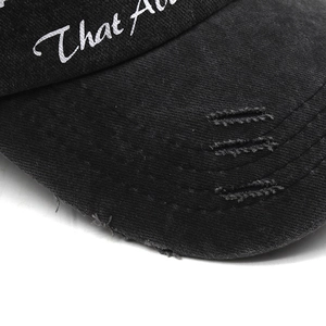 Macro detail of distressed brim on black cotton baseball cap with white embroidery
