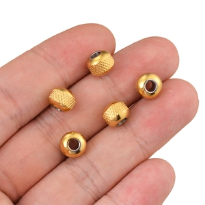 Knurled golden stainless steel cylindrical beads shown on palm for scale