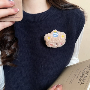 Close-up of a flocking bear brooch with a striped hat on a dark blue knitted vest