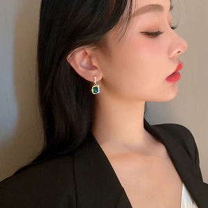 Close-up of elegant gold earrings with square green gemstones and sparkling rhinestones