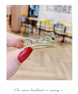 Close-up of golden metal hair clip with green accents held by hand in a cozy cafe setting
