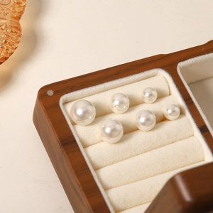 Detail of solid wood jewelry storage box with velvet slots holding white pearl earrings