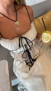 Close-up of white layered ruffle dress with black trim and delicate layered necklaces