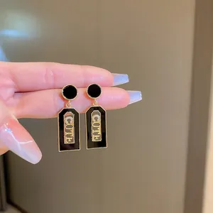 Detail of black and gold drop earrings featuring CUTE letters with sparkling zircons