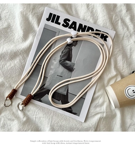 Close-up of woven cream shoulder strap with brown details and metal rings on a white background
