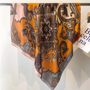 Detail of warm orange paisley satin scarf draped on a metal rod with silk gloss