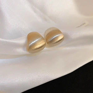 Detail of gold brushed metal earrings with thick curved design on white silk background