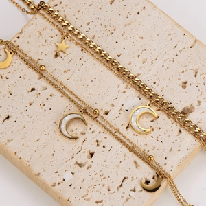Golden double-layer stainless steel necklace featuring star and moon pendants on travertine