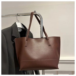 Detail of a large dark brown leather tote bag hanging on a rack next to a black blazer