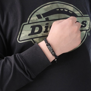 Close-up of woven bracelet with engraved stainless steel plate on person's wrist
