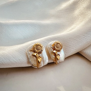 Macro detail of golden sunflower earrings with baroque pearls on white silk fabric
