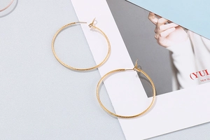 Close-up of gold hoop earrings featuring elegant spiral texture on a gray textured background