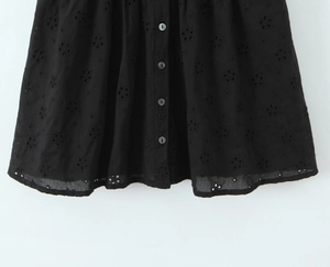 Détail de la jupe en coton noir avec broderie florale et quatre boutons à l'avant
