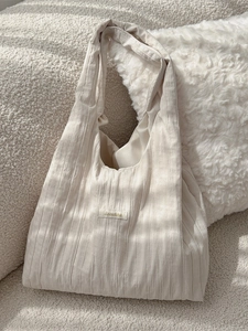 Minimalist cream pleated shoulder bag with brand label on a textured sofa setting