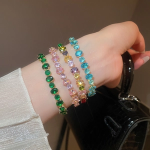 Vue du poignet de quatre bracelets de luxe en zircon émeraude, rose, bleu et monture dorée
