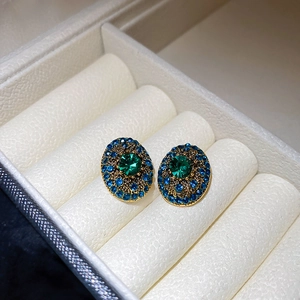 Detail of vintage oval gold earrings with green center stone and blue crystals