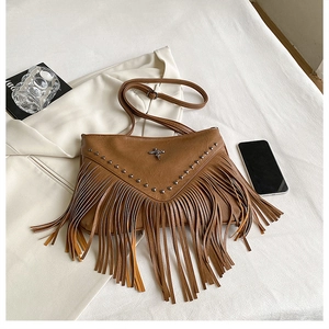 Détails d'un sac bandoulière marron avec rivets, emblème en croix et longues franges