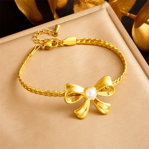 Detailed view of gold braided chain bracelet with pearl bow accent on textured display