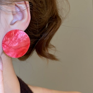 Close-up of a large red circular acrylic earring with sequins worn by a female model