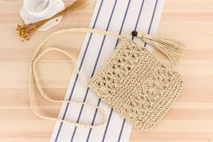 Detail of hollow woven floral pattern on a beige straw bag with long fringe tassels