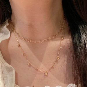 Collana a doppio strato dorata con maglie vuote, ciondoli a cuore e strass incastonati