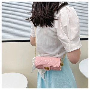 Detail of pink quilted cylinder bag with gold chain strap worn by a model