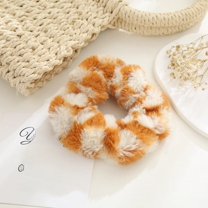 Close-up of orange checkerboard plush scrunchie on a warm lifestyle background
