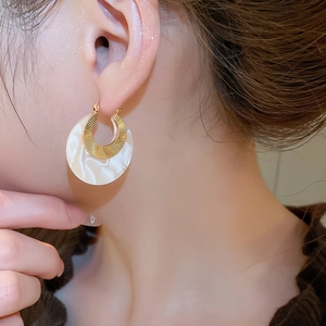 Close-up of golden radial ring and marbled acetate crescent earring worn by model