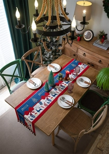 Christmas table runner with reindeer motifs and decorative tassels on a wooden dining table